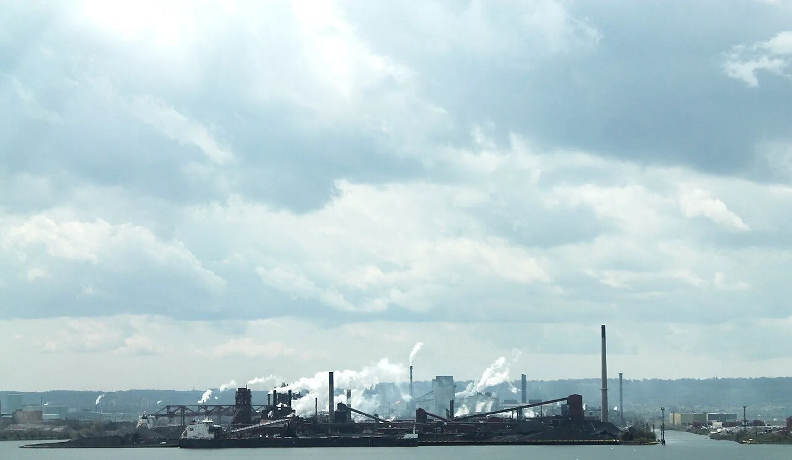 Steel mill waterfront with ore piles and smokestacks. Trump announced a $15-18 billion integrated steel plant and iron-o